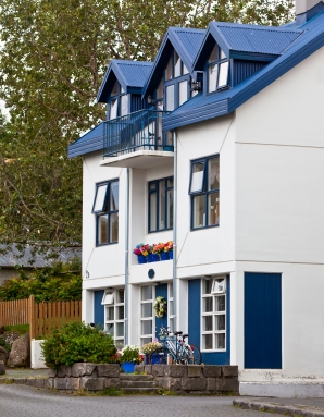 Nowoczesny biały dom z niebieskimi elementami i dużą ilością roślinności wokół.